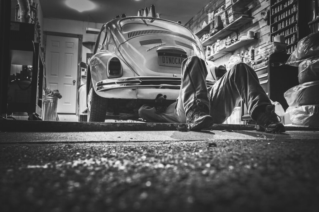 collection-05 Mechanic working beneath a classic Volkswagen Beetle in a vintage garage setting.