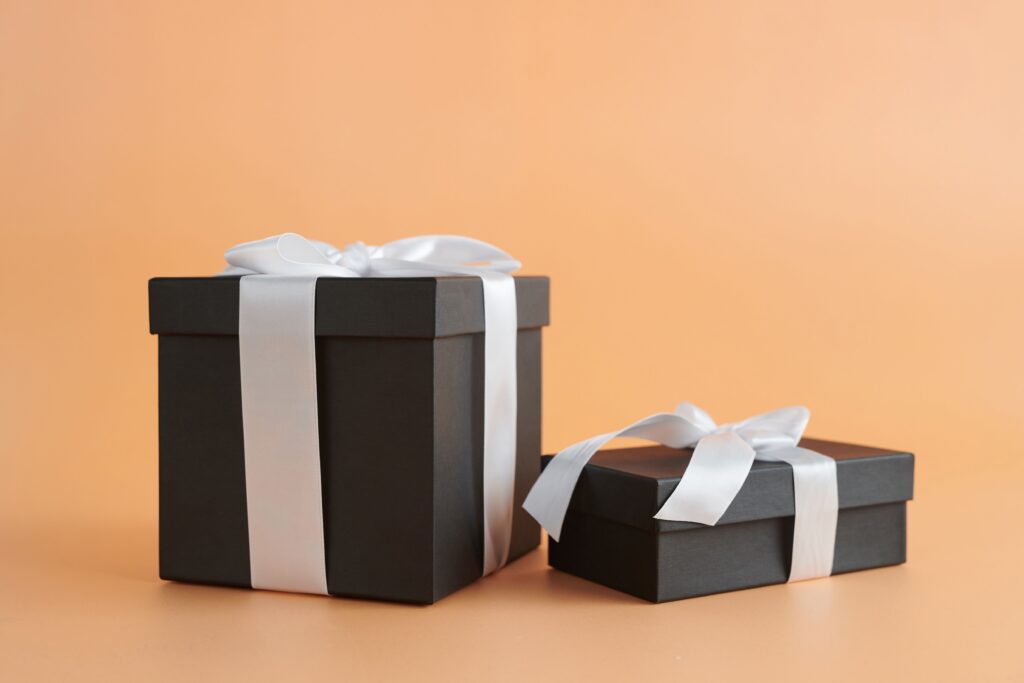 collection-02 Two black gift boxes with white ribbons on a beige background, perfect for celebrations.