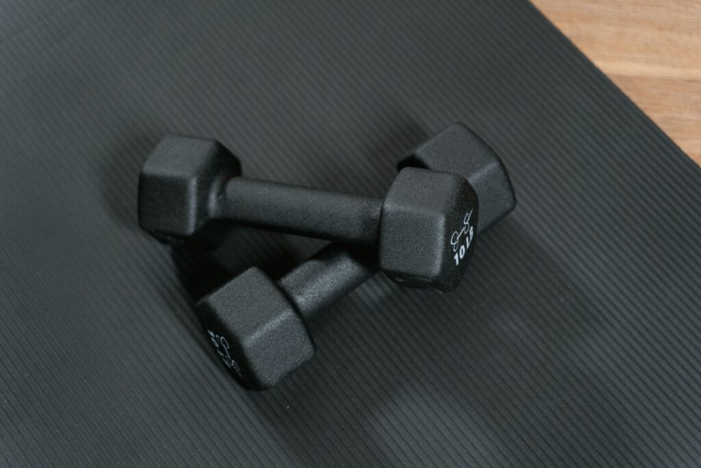 collection-04 Black dumbbells placed on a yoga mat, perfect for home workouts and strength training.