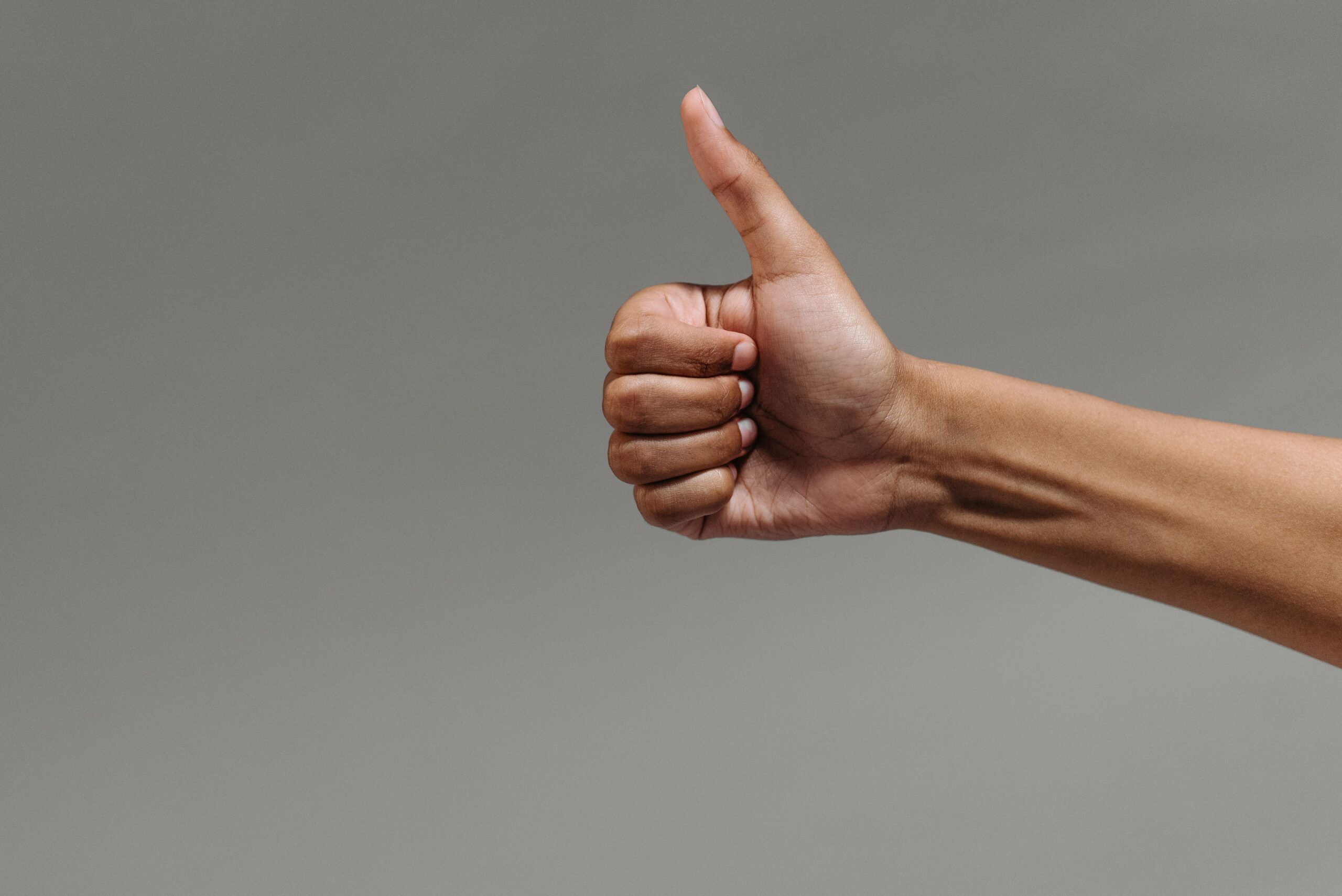 about-us-02 A close-up image of a hand making a thumbs up gesture against a neutral background.
